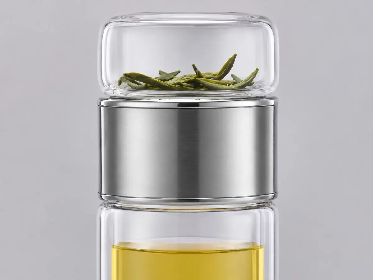 Close-up of the brushed steel collar of the glass bottle, green leaves in the chamber above and amber tea below