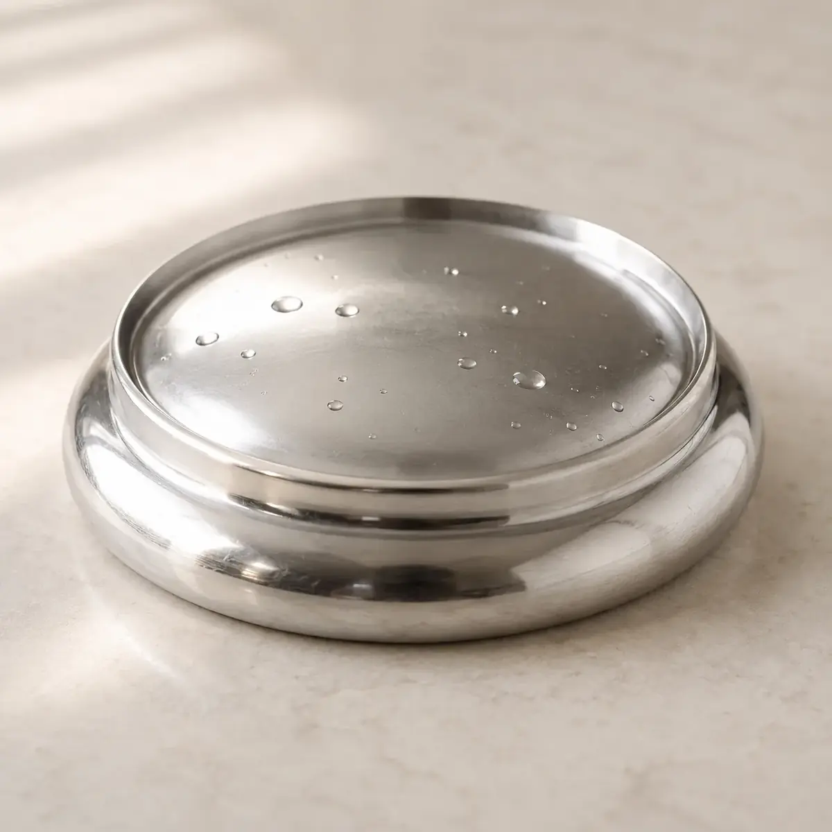 Close-up of the polished domed steel lid resting upside down with water droplets on it