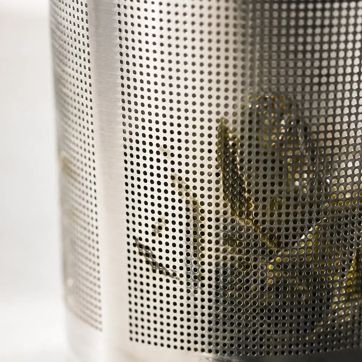 Extreme close-up of the fine perforated mesh of a steel tea infuser with green leaves visible behind it
