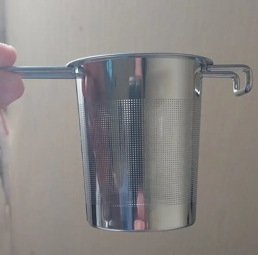 A hand holding the steel infuser basket by one long handle, mesh wall catching the light. Photographed by R***a, a verified buyer