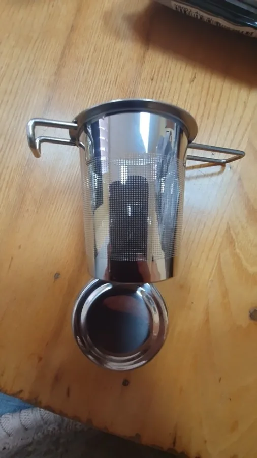 The steel infuser basket photographed from above on a light wooden table. Photographed by P***a, a verified buyer