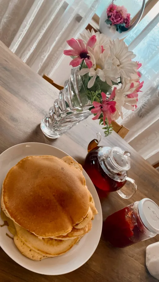 The glass teapot of red tea on a breakfast table beside pancakes and flowers. Photographed by Y***n, a verified buyer
